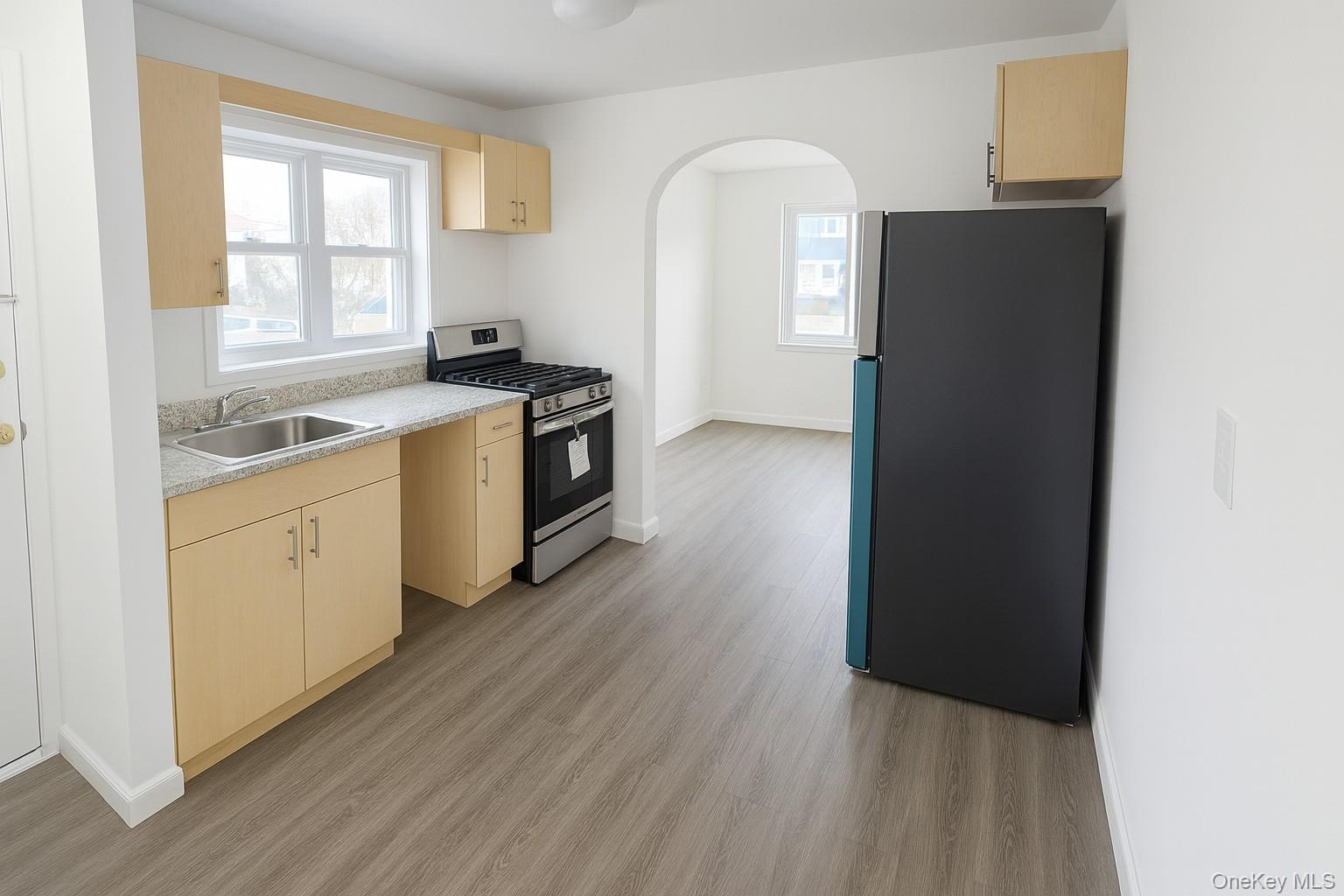 Kitchen with light brown cabinets, appliances with stainless steel finishes, light countertops, and arched walkways