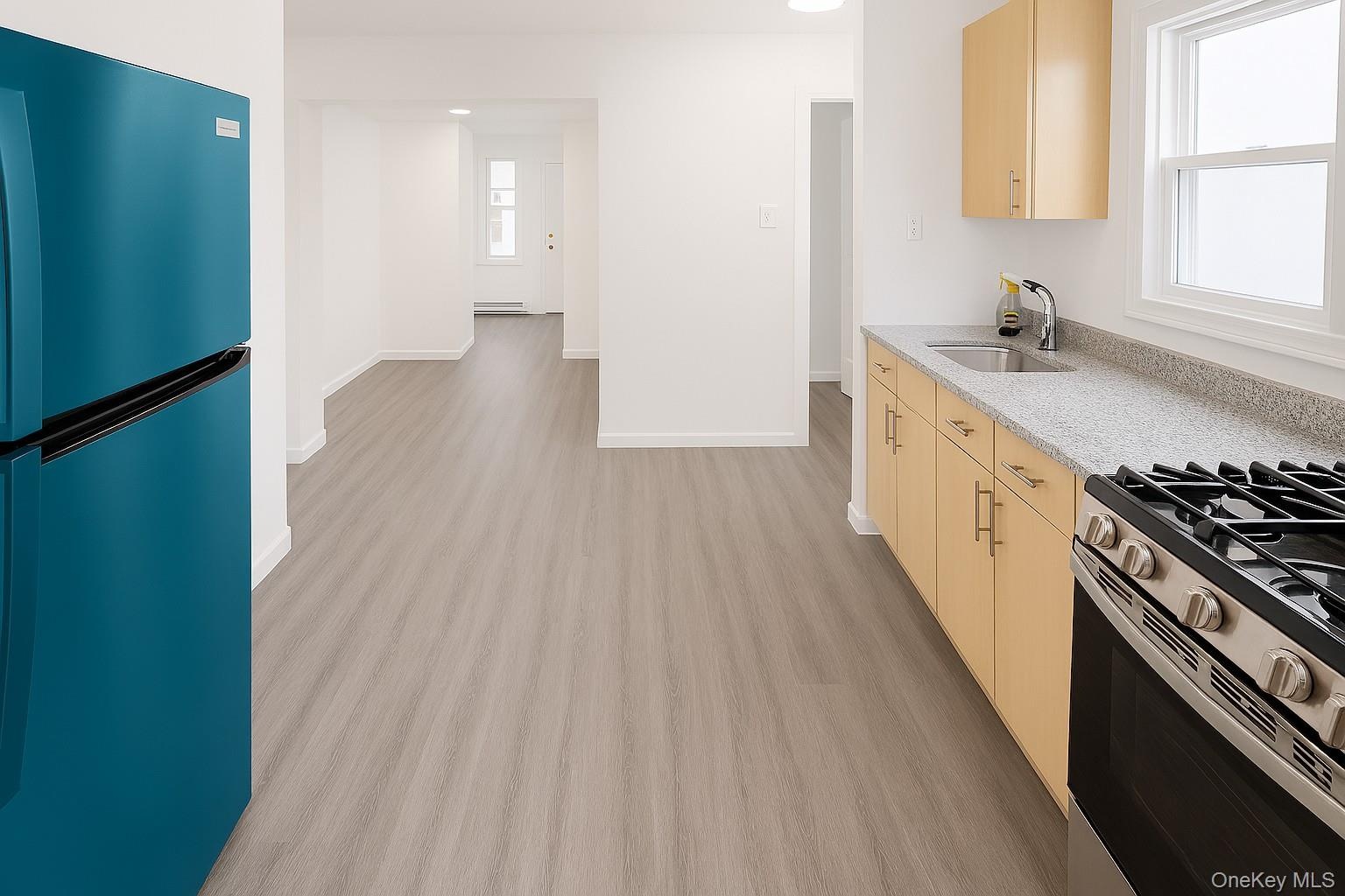 Kitchen featuring freestanding refrigerator, light brown cabinetry, light stone countertops, and gas range