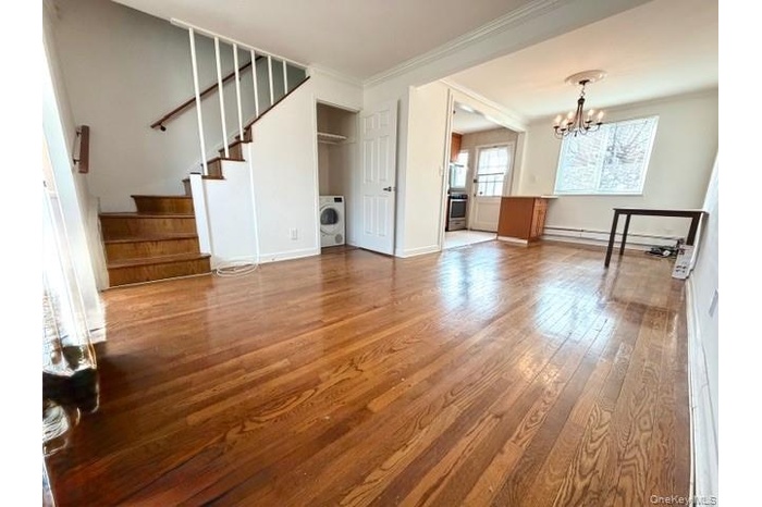 Unfurnished living room featuring stairs, crown molding, light wood-type flooring, a chandelier, and a baseboard heating unit