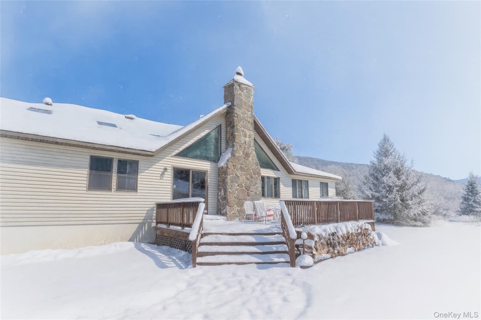Snow covered back of property with a deck and a chimney