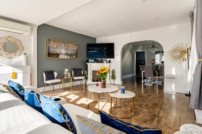 Living room with arched walkways, wood finished floors, a fireplace with raised hearth, and a wall mounted AC