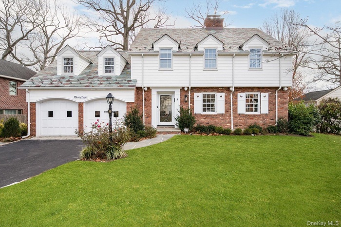 View of front facade with driveway, brick siding, a front yard, a chimney, and a high end roof