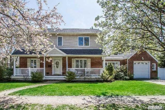 View of front facade with covered porch, a front yard, a garage, and brick siding