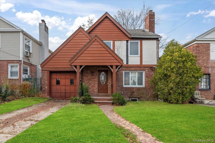 View of front of home with brick siding, a front yard, driveway, and a chimney
