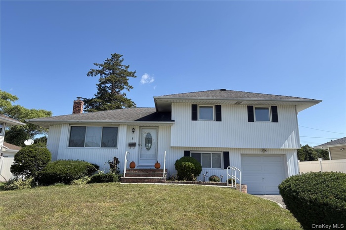 Tri-level home featuring a garage, a chimney, and a shingled roof
