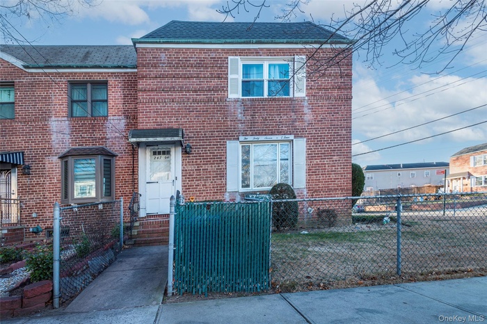 Traditional-style house featuring a shingled roof, brick siding, and a fenced front yard
