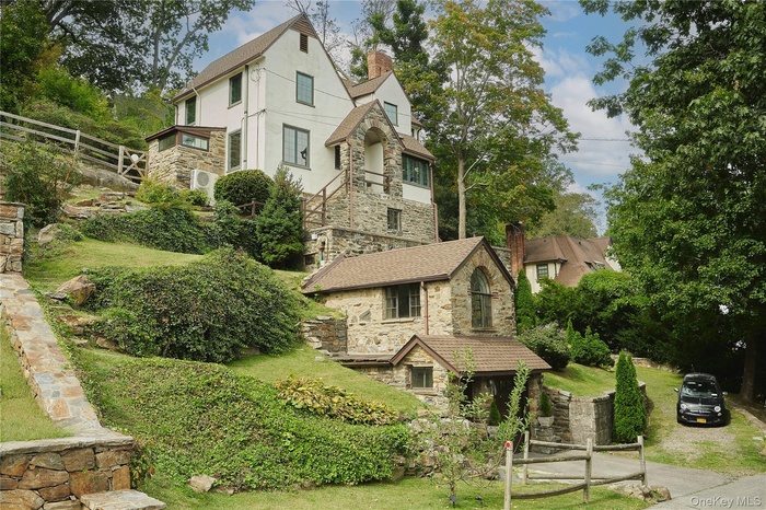 Tudor-style house featuring stone siding, a chimney, stucco siding, and view of scattered trees