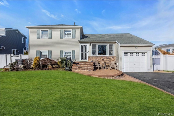 Tri-level home featuring an attached garage, driveway, stone siding, and roof with shingles