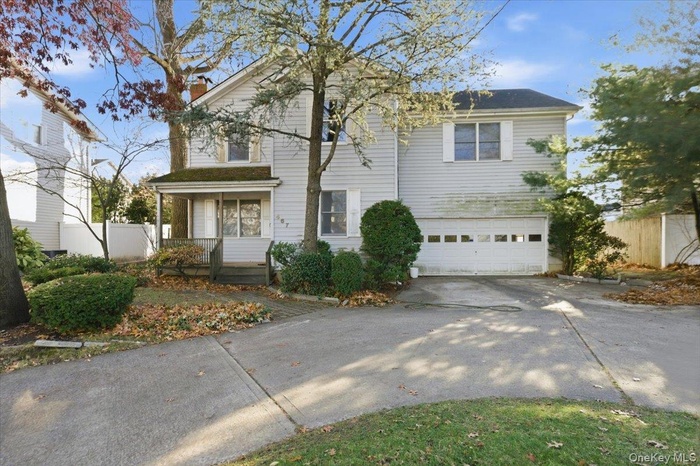 Traditional-style home featuring covered porch, concrete driveway, an attached garage, and a chimney