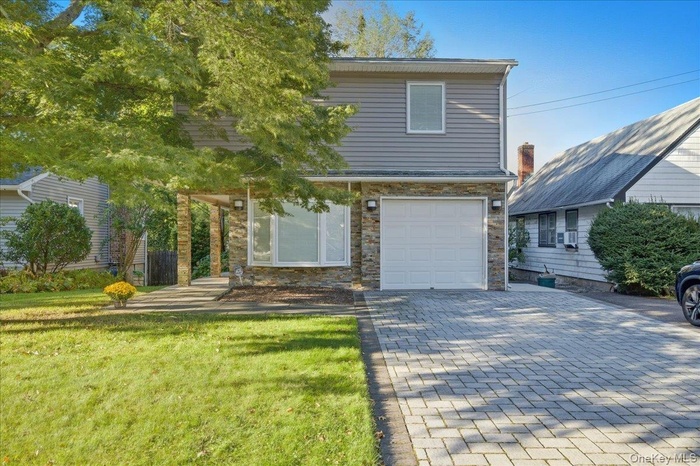 Traditional-style home with a front lawn, decorative driveway, stone siding, and a garage