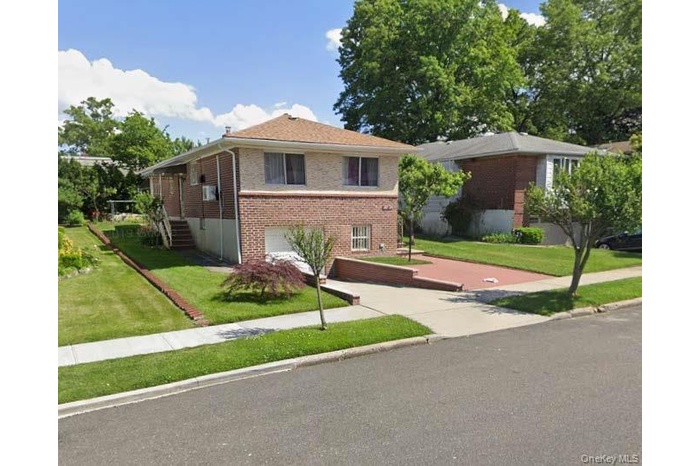 View of front facade featuring a front yard, brick siding, driveway, and a garage