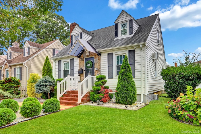 New england style home featuring a front yard, stone siding, roof with shingles, and a chimney