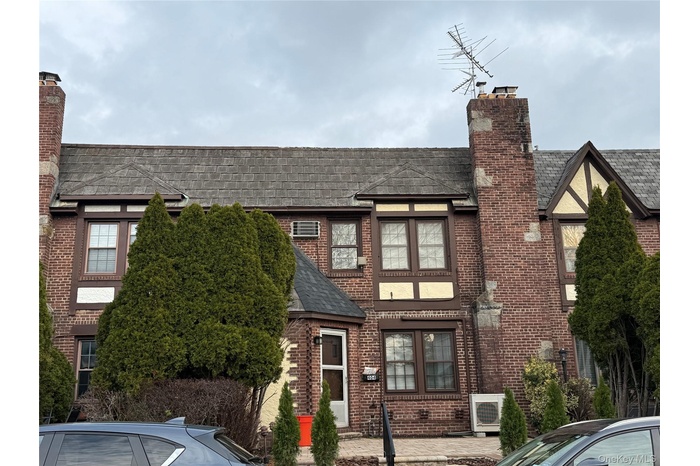 Tudor-style house with a chimney, roof with shingles, and brick siding