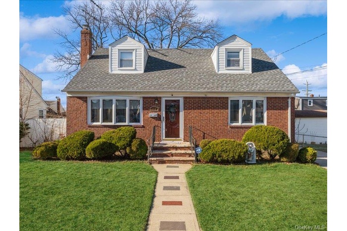 Cape cod house with brick siding, a chimney, and roof with shingles