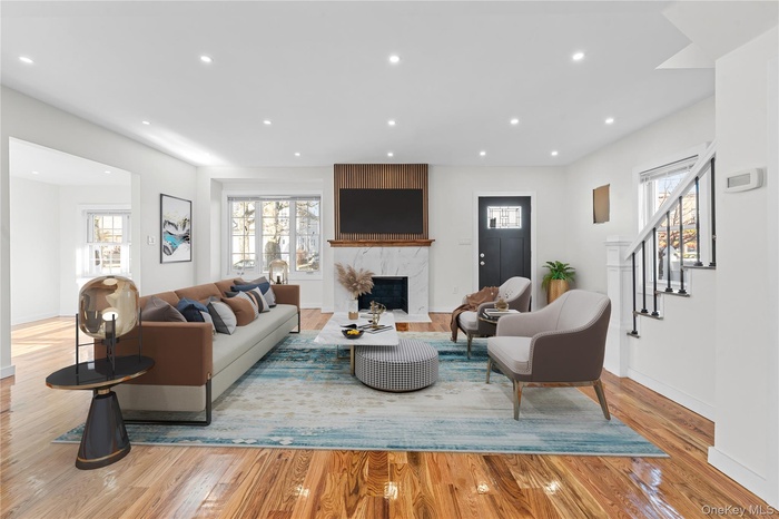Living room with a premium fireplace, stairway, light wood finished floors, and recessed lighting