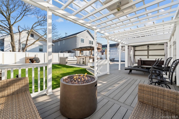 Wooden deck featuring a fire pit, a fenced backyard, a pergola, and an outdoor kitchen