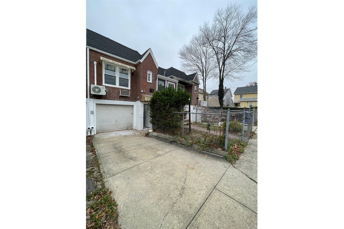 View of side of home featuring concrete driveway, brick siding, a fenced front yard, an attached garage, and a wall mounted air conditioner