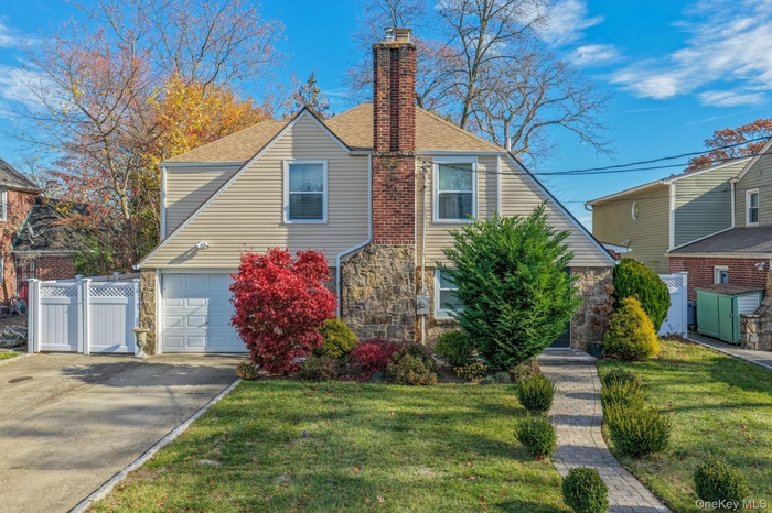 View of front of house with roof with shingles, stone siding, a chimney, driveway, and an attached garage
