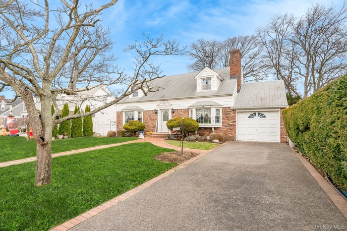Cape cod home featuring a front lawn, a shingled roof, brick siding, and driveway