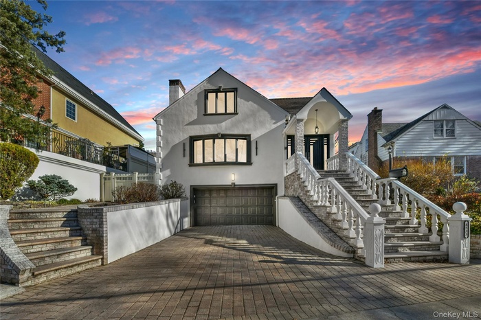 View of front of property with stucco siding, a garage, decorative driveway, a chimney, and stairs