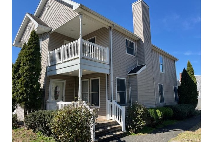 Rear view of property featuring covered porch, a chimney, and a balcony