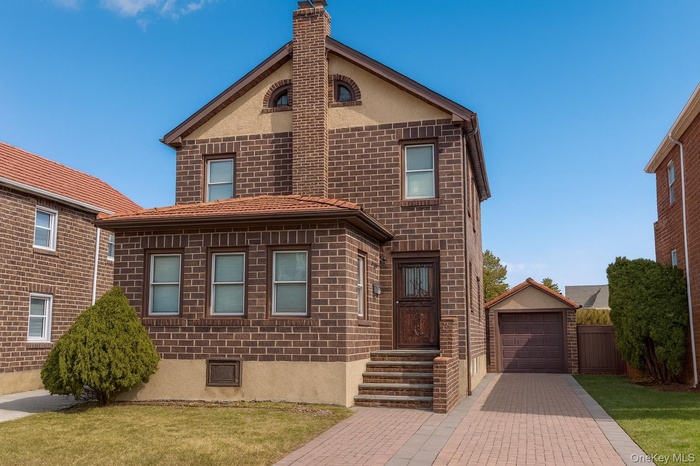 View of front of house with driveway, brick siding, a detached garage, stucco siding, and an outbuilding