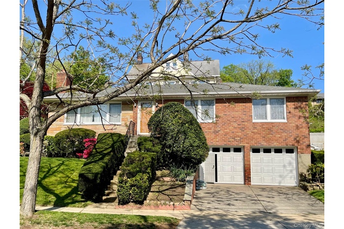 View of front of house featuring brick siding, driveway, an attached garage, and a chimney
