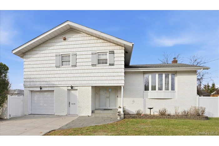 Split level home featuring brick siding, an attached garage, a chimney, and concrete driveway