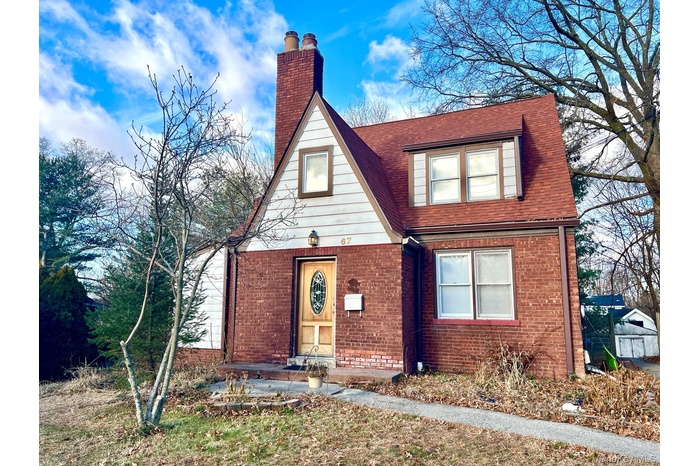 View of front facade featuring brick siding, a shingled roof, and a chimney