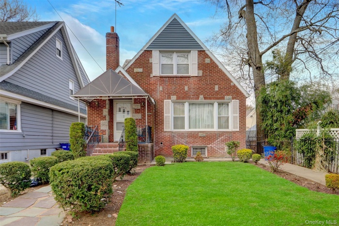 English style home featuring a chimney, a front lawn, brick siding, and fence