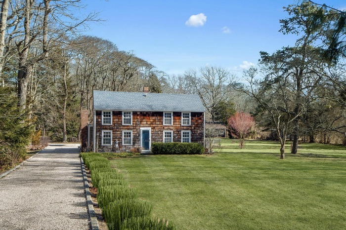 View of front facade featuring a chimney, a shingled roof, gravel driveway, and a front lawn