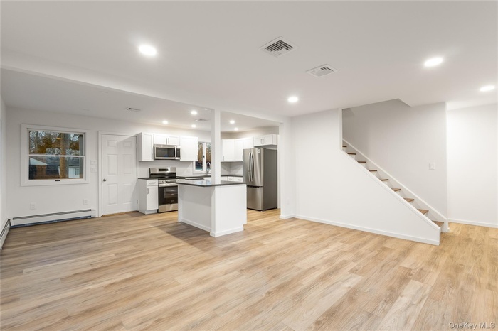 Kitchen featuring open floor plan, white cabinets, stainless steel appliances, a center island, and light wood-style floors