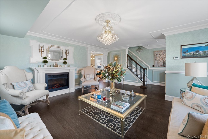 Living room featuring a fireplace, stairs, a chandelier, dark wood-style HEATED flooring, and crown molding, wainscoting