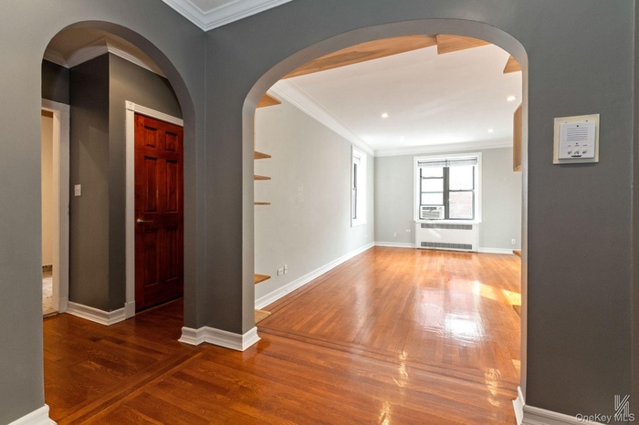 Hall featuring crown molding, arched walkways, wood finished floors, and radiator heating unit