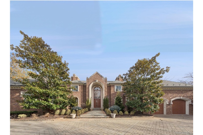View of front of home with brick siding, driveway, a chimney, and a garage