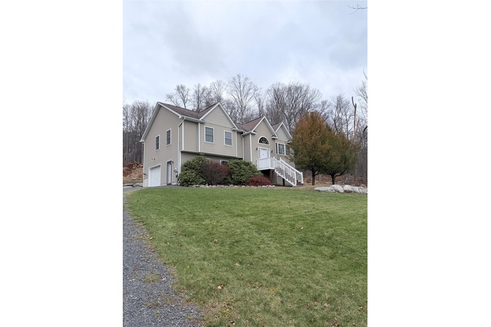 View of front of home featuring a garage, a front lawn, driveway, and a wooden deck