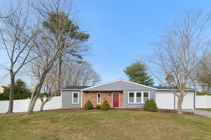 Ranch-style home featuring a garage, a chimney, driveway, and brick siding