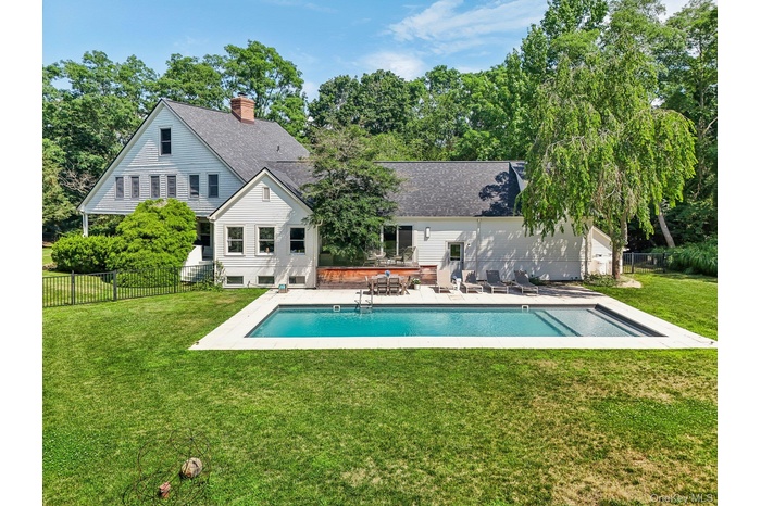 Rear view of house featuring a patio, a fenced backyard, a chimney, roof with shingles, and view of scattered trees