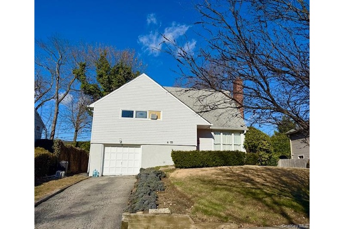 View of property exterior with driveway, a chimney, and a garage