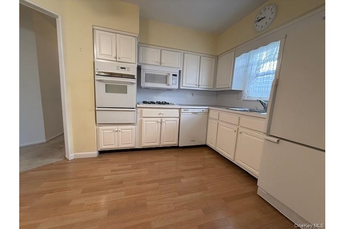 Kitchen with white cabinets, white appliances, light countertops, and light wood finished floors