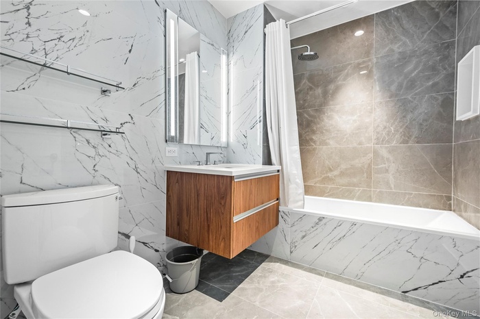 Full bath featuring vanity, tiled shower / bath, tile walls, and light marble finish flooring