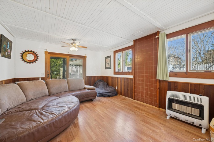 Living room with wood walls, wood ceiling, healthy amount of natural light, heating unit, and wainscoting