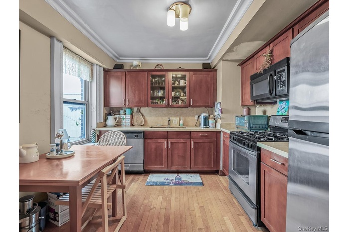 Kitchen featuring stainless steel appliances, light countertops, glass insert cabinets, crown molding, and light wood finished floors