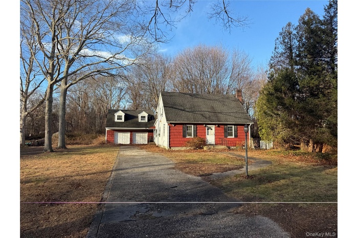 Cape cod-style house with roof with shingles, a front yard, asphalt driveway, a chimney, and a garage