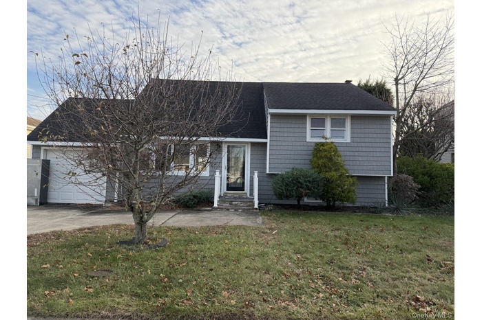 Tri-level home with a shingled roof, a front yard, driveway, and an attached garage