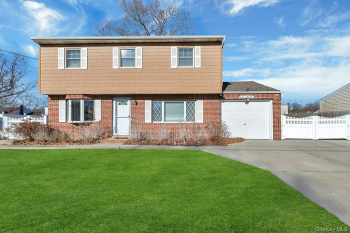 Colonial-style house featuring driveway, a garage, brick siding, and roof with shingles