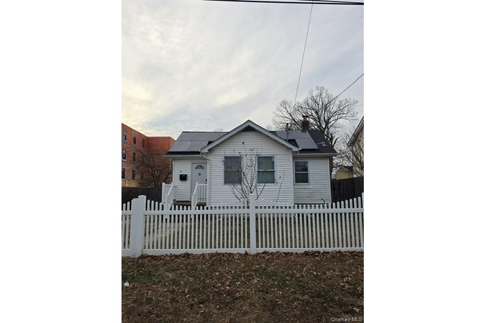 Bungalow-style home featuring a chimney, solar panels, and a fenced front yard