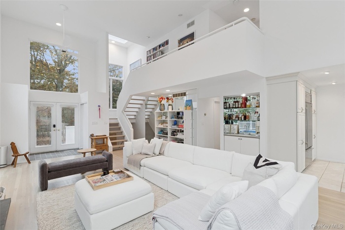 Living area with a towering ceiling, light wood-style floors, french doors, stairway, and recessed lighting