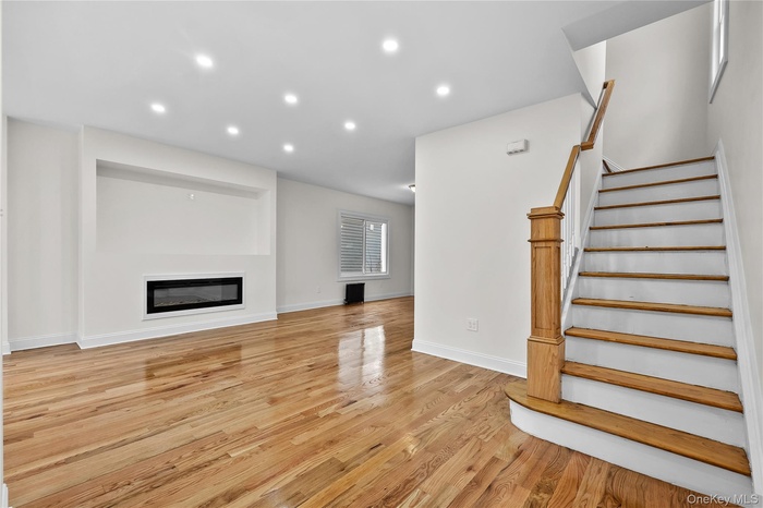 Unfurnished living room with a glass covered fireplace, recessed lighting, light wood finished floors, and stairs