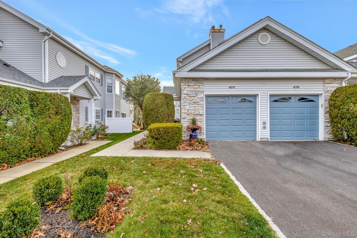 View of front of home featuring asphalt driveway, stone siding, a chimney, a front lawn, and a garage